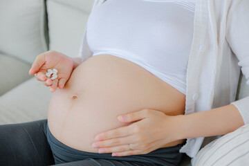 Close up hand of Asian happy pregnant woman with medicine on sofa and touching her belly. Family...
