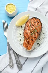 Tasty grilled salmon steak with rice, thyme, lemon and sesame seeds served with sauce on light blue wooden table, flat lay