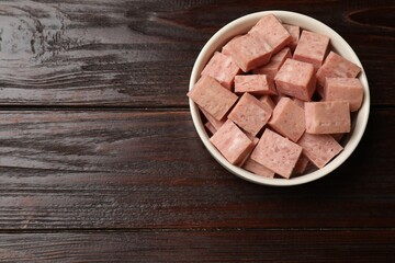 Pieces of canned meat in bowl on wooden table, top view. Space for text