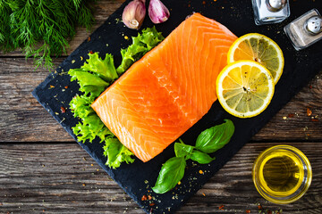 Fresh raw salmon steak with fresh vegetables on black stony board on wooden background
