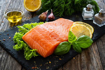 Fresh raw salmon steak with fresh vegetables on black stony board on wooden background
