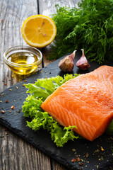 Fresh raw salmon steak with fresh vegetables on black stony board on wooden background
