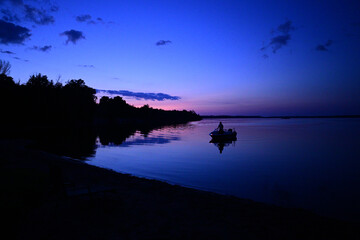 Evening landscape of a fishing boat coming to shore as the sun sets on the horizon 