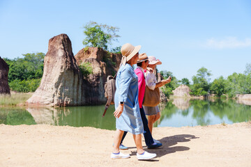 Three senior women friends walking beside a scenic lake surrounded by rock formations, enjoying a...