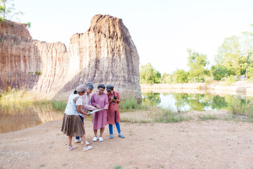 Senior women friends gathering around a map, planning their route in a scenic natural area with rock formations. Their relaxed outfits and focused expressions show enjoyment in outdoor exploration.