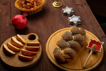 Homemade challah, honey, apple and pomegranate and burning candles on the table with a menorah Rosh...