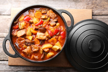 Delicious stew with vegetables in pot on wooden table, top view