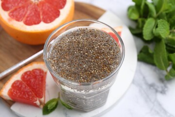 Glass of drink with chia seeds and grapefruit on white marble table, closeup