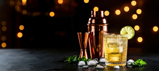 Chic Cocktail Glass with Copper Shaker and Lime Garnish in Festive Setting on dark background, banner.International Bartender's day Concept