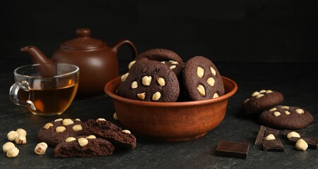 Tasty chocolate cookies with hazelnuts and tea on black table