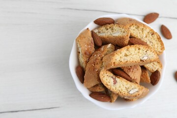 Tasty almond biscuits (Cantuccini) and nuts in bowl on white wooden table, top view. Space for text