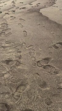 A serene beach on the Curonian Spit, marked by footprints trailing along the sandy shore, captures the essence of a peaceful walk by the sea. Gentle waves lap against the coastline under an overcast