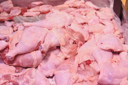 a pile of raw chicken pieces, primarily consisting of chicken legs and thighs. The chicken pieces are displayed in a market or store setting, likely for sale. - Powered by Adobe
