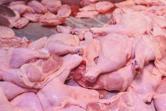 a pile of raw chicken pieces, primarily consisting of chicken legs and thighs. The chicken pieces are displayed in a market or store setting, likely for sale.