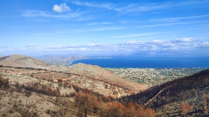 Photo of the charred slopes of Mount Pentelicus in Dionysos, with a view over the scenic coastal town of Nea Makri in East Attica, Greece. The landscape showcases the extensive damage in the area.