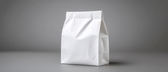 A minimalist white paper bag stands upright against a gray background, emphasizing its simple design and potential for versatile use.