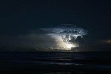 Thunderstorm cell over the sea at night with visible stars in the sky, creating a dramatic scene