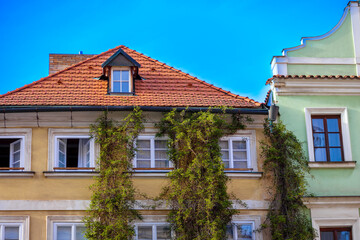
a yellow building with a red tiled roof and a creeper on the wall
