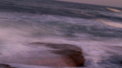 Slow shutter speed photo of ocean water flowing over a rock, located at orange rocks in Margate South Africa