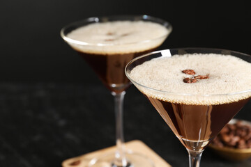 Delicious espresso martini with coffee beans in glasses on blurred black background, closeup