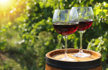 Tasty wine in glasses on wooden barrel outdoors. Space for text