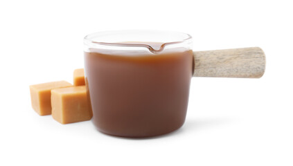 Tasty caramel sauce in glass measuring cup and sweet candies isolated on white