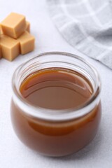Tasty caramel sauce in jar and candies on light table, closeup