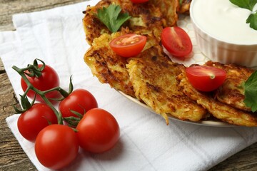 Delicious potato pancakes, sour cream, tomatoes and parsley on wooden table, closeup