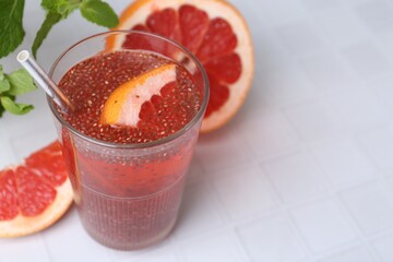 Glass of drink with chia seeds and grapefruit on white tiled table, closeup. Space for text