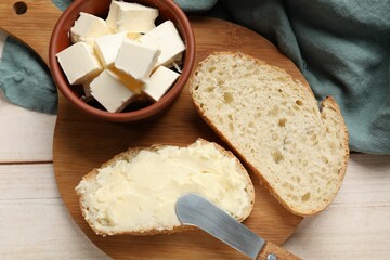 Fresh bread with butter and knife on light wooden table, top view