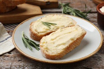 Fresh bread with butter and rosemary on wooden table, closeup