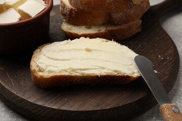 Fresh bread with butter and knife on grey table, closeup