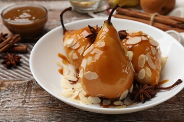 Delicious pears with caramel sauce, almond flakes and spices on wooden table, closeup
