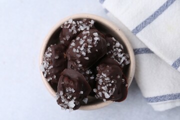 Tasty chocolate candies with salt in bowl on light table, top view
