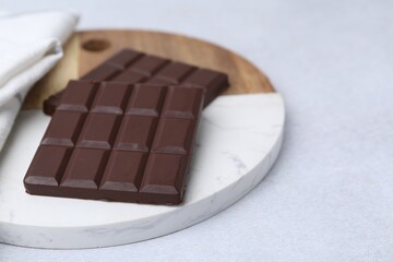 Pieces of delicious dark chocolate bar on light table, closeup. Space for text