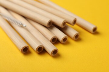 Bamboo drinking straws and cleaning brush on yellow background, closeup