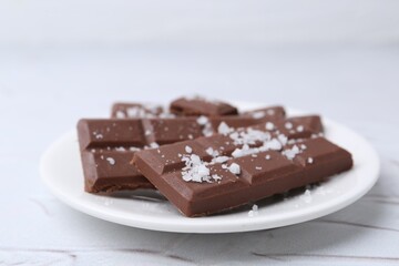 Pieces of chocolate with salt on white table, closeup