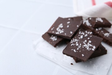 Pieces of chocolate with salt on white table, closeup. Space for text