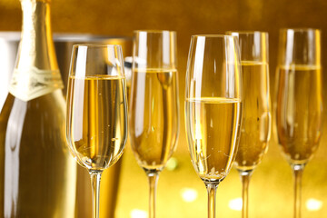 Champagne in glasses, bottle and ice bucket on golden background, closeup