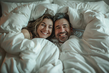 Middle aged couple having fun laughing under duvet in bed at home