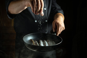 In a dimly lit kitchen, a chef expertly sprinkles salt over fresh shrimp in a hot pan, creating an inviting atmosphere filled with anticipation of delicious flavors