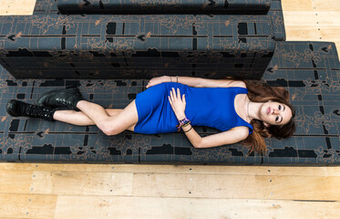 Portrait of an 18 year old white woman, in a blue short dress, lying on a grey couch, view from above