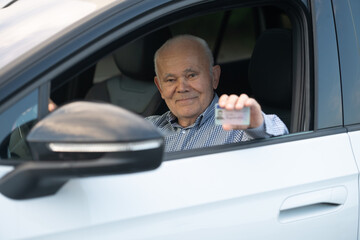 Elderly Man Proudly Displaying Driver’s License from Car Window