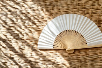 Minimalist image of a traditional hand fan casting intricate shadows on a woven wicker background