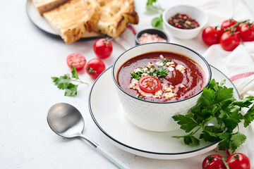 Tomato puree soup garnished with parsley, feta cheese and spices with toasted bread slices, tomatoes and herbs on white table