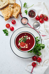 Tomato puree soup garnished with parsley, feta cheese and spices with toasted bread slices, tomatoes and herbs on white table
