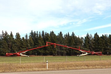 Two grain augers placed in front of a tree line facing in a way to form an arch.