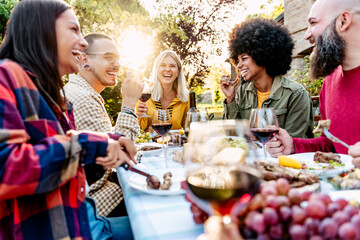 Young friends having fun drinking red wine on balcony at house dinner pic nic party - Hipster millennial smiling people eating bbq food at fancy restaurant together - Dining home lifestyle concept