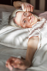 Happy middle aged woman sits on bed and stretching arms