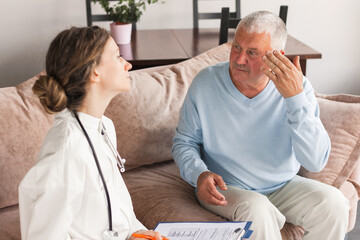 Female professional doctor showing medical test result explaining prescription using clipboard visiting senior elderly old man patient at home sitting on sofa